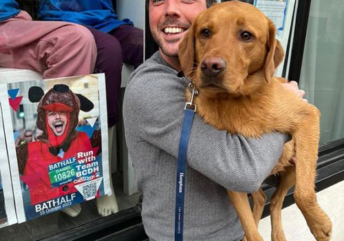 Dan Hill and his dog Basil outside our Charity Shop window featuring him running the Bath Half last year